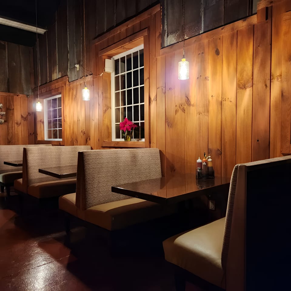 Cozy restaurant interior with wooden walls, booth seating, and warm lighting from hanging lamps.
