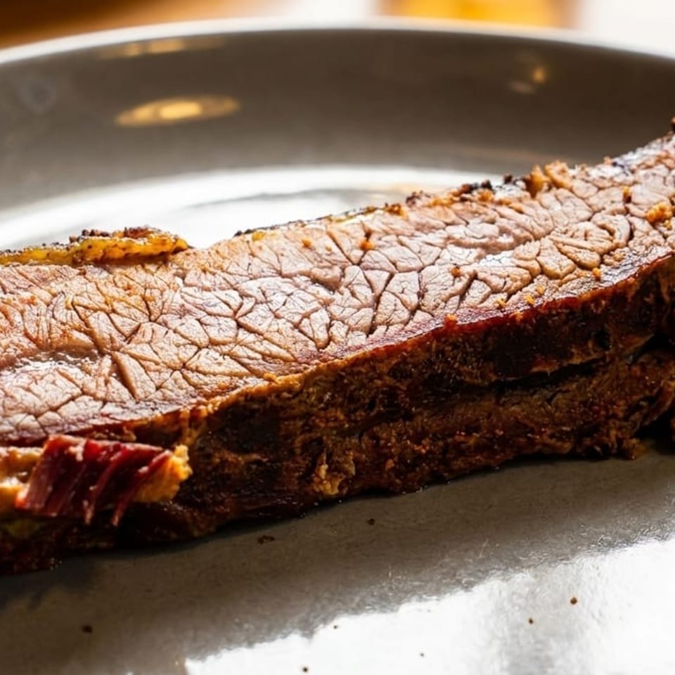 Thick sliced barbecue beef brisket with a browned crust served on a gray plate alongside barbecue sauce.