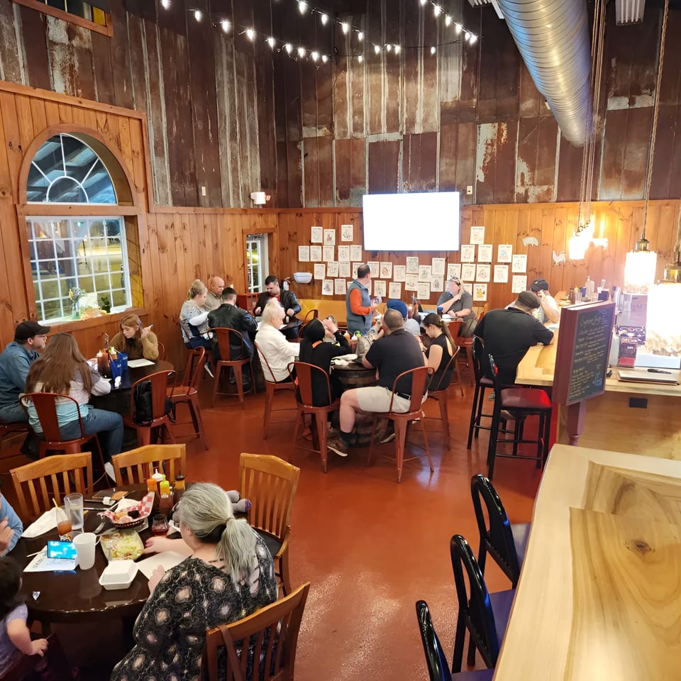 A rustic restaurant interior with wooden walls, string lights, and patrons dining at tables.