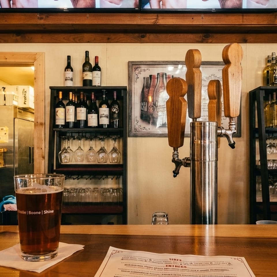 A beer on a wooden bar counter with taps, wine bottles, and glasses in the background.